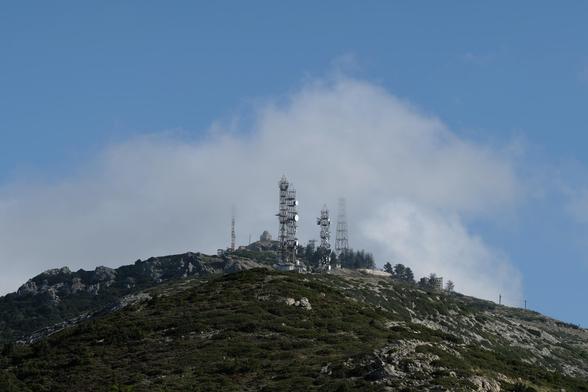 Photo of a mountain top with several antennae and a small chapel partly shrouded in clouds.