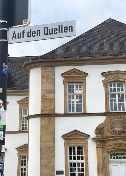 Im Vordergrund neues Straßenschild mit der Aufschrift "Auf den Quellen", im Hintergrund Frontansicht der Zentralbibliothek Paderborn
