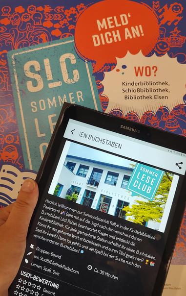 Werbung für eine Veranstaltung des Sommerleseclubs: Ein Tablet zeigt eine digitale Rätsel-Rallye der Stadtbibliothek Paderborn. Im Hintergrund sind ein "Sommer Lese Club" Plakat und die Aufforderung "Meld dich an!" zu sehen.