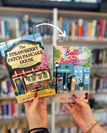 Zwei Hände halten vor einem unscharfen Bücherregal zwei Romane. Links ist „The Strawberry Patch Pancake House“ von Laurie Gilmore zu sehen, rechts „Battle of the Bookstores“ von Ali Brady. Ein weißer, gebogener Pfeil zeigt vom linken auf den rechten Roman.